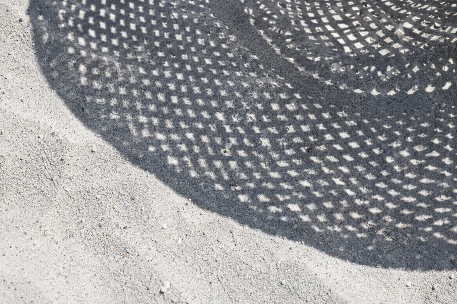 Shadow of a woven hat on pale sand